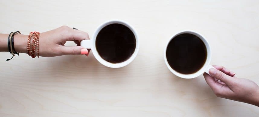 Two hands holding cups of black coffee on a white table