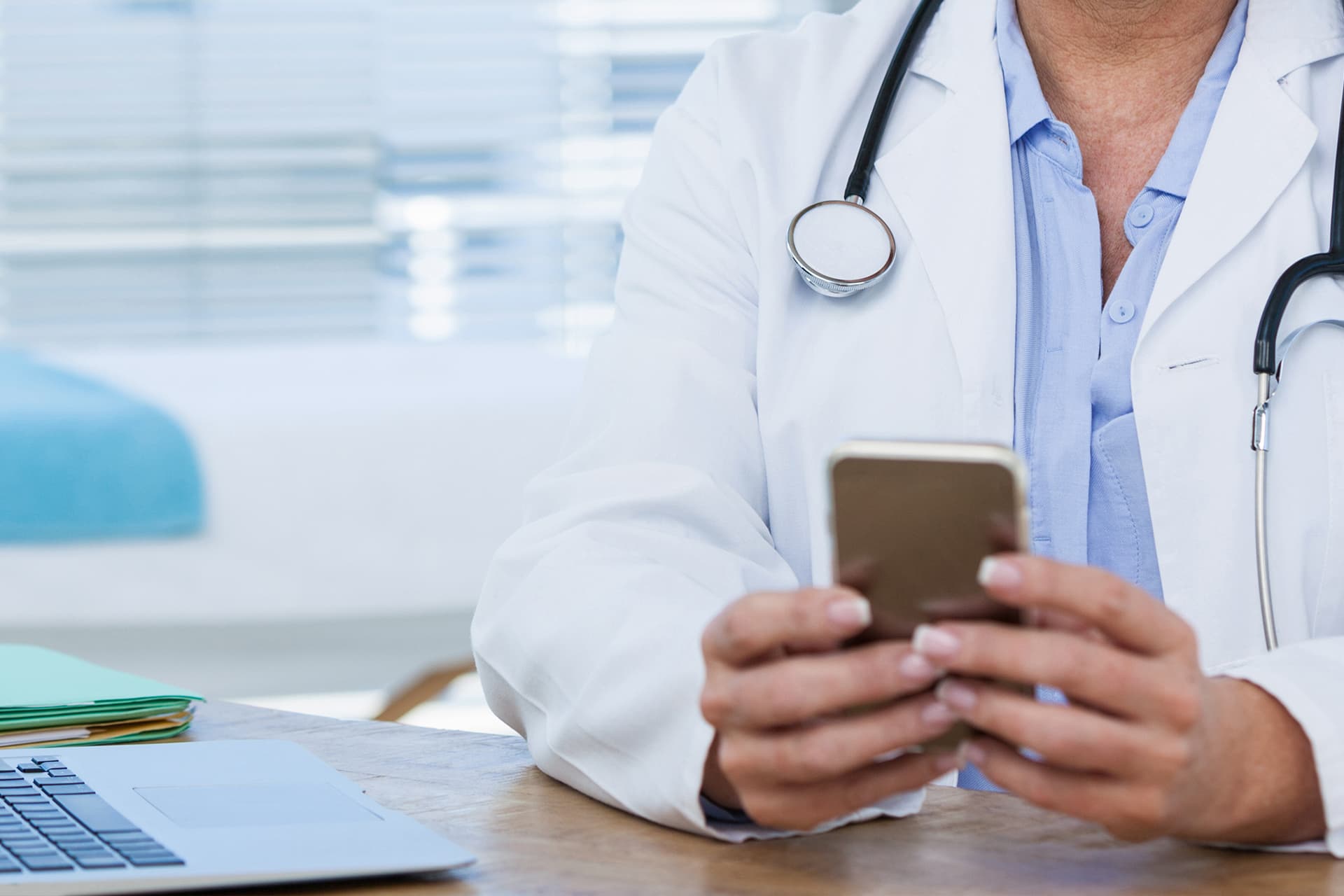 A doctor in a white coat using a smartphone at a desk
