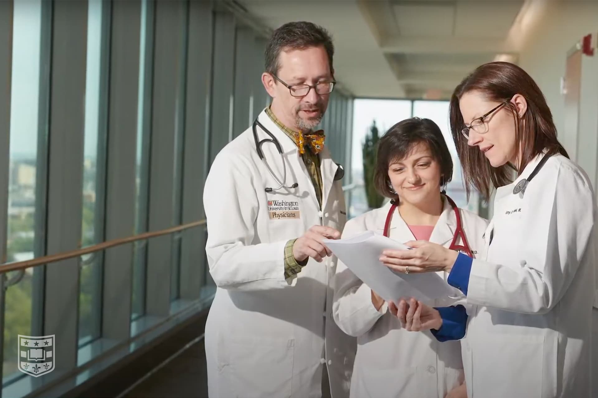 Three doctors in white coats reviewing a document in a hospital hallway