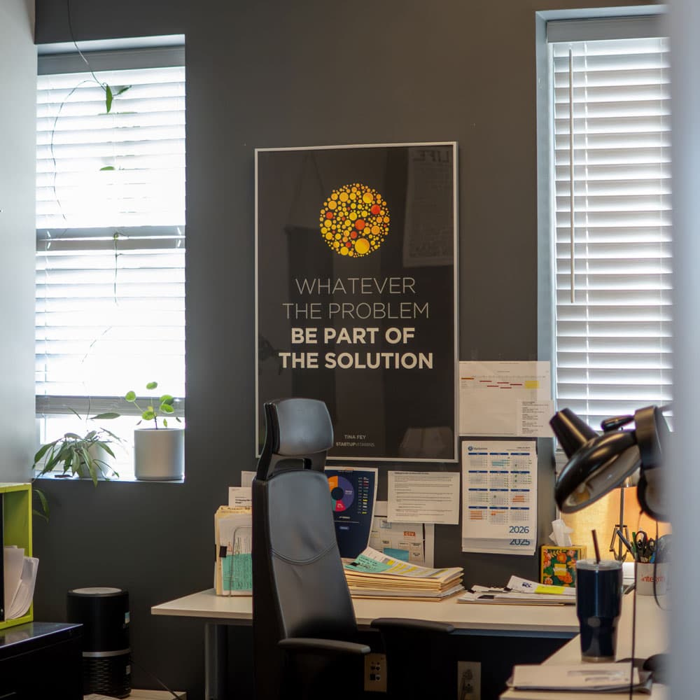 Office desk under a poster reading “Whatever the problem, be part of the solution”