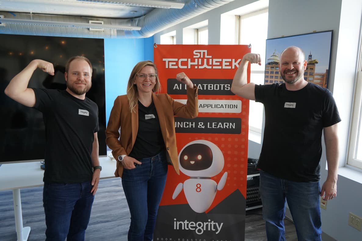 Three team members flexing in front of an STL TechWeek AI chatbot lunch-and-learn banner