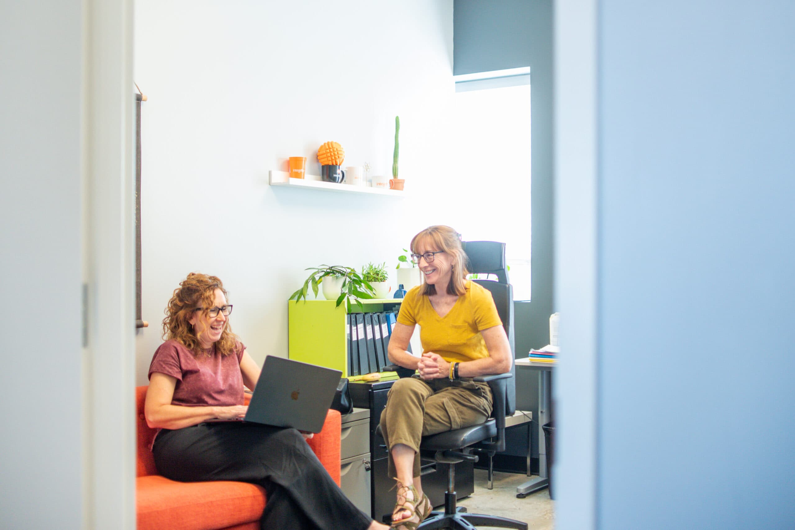 Two team members talking in a small office, one with a laptop