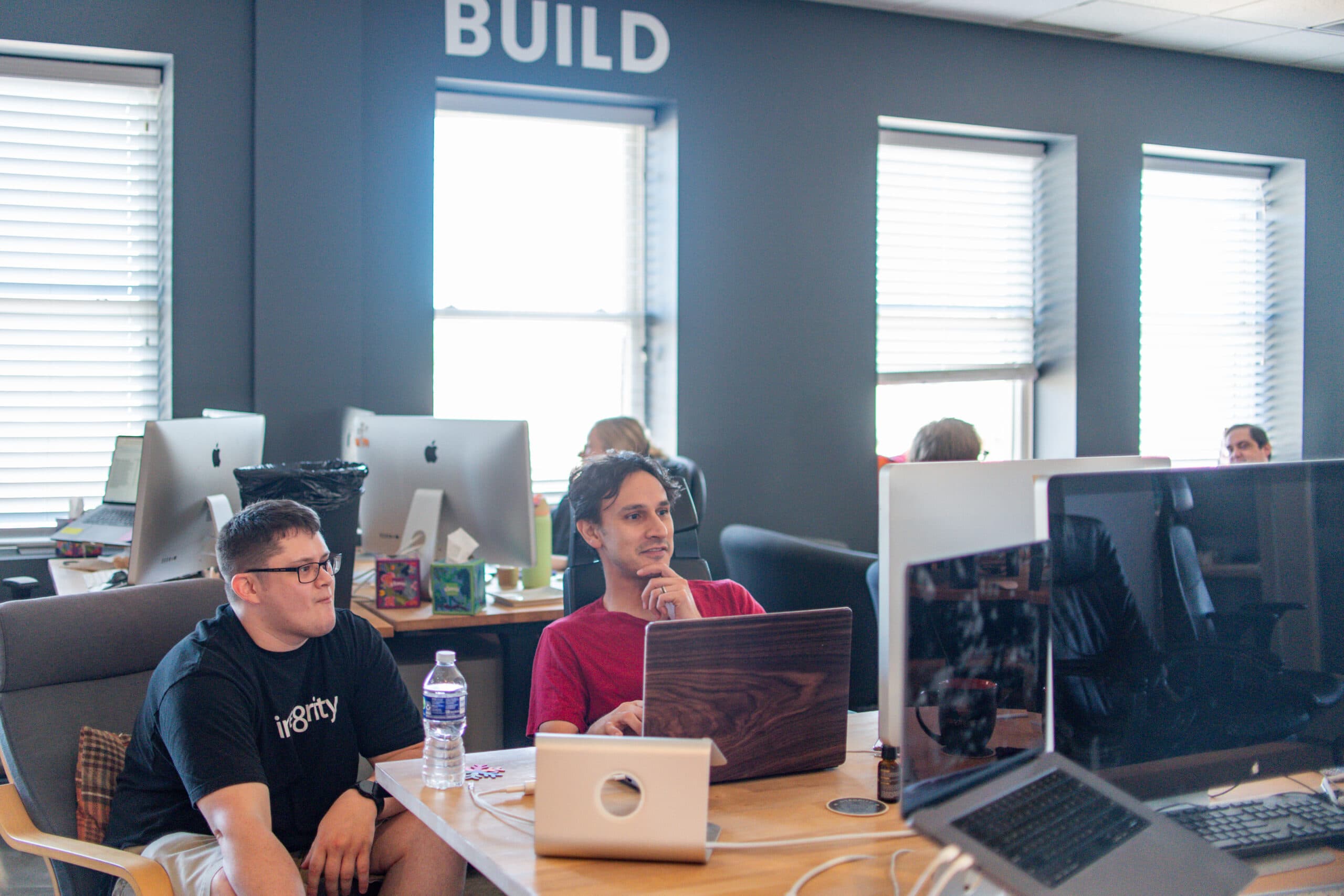Team members working at desks under a wall that reads Build